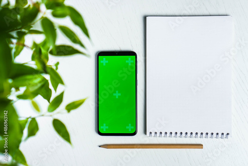 Green leave with blank notepad smartphone green screen mockup and pencil flat lay. Top view