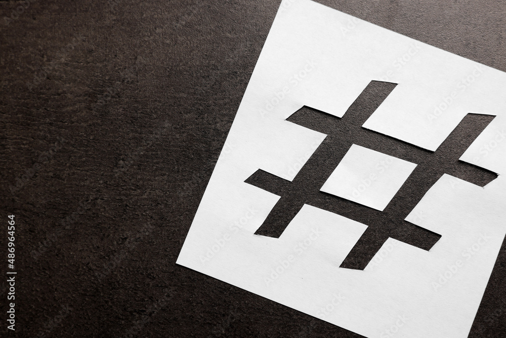 Obraz premium White paper stencil with symbol of hashtag on dark background, top view. Space for text