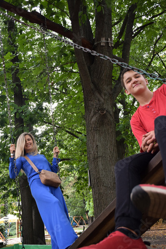 A guy and a young woman ride on a swing in an amusement park and smile