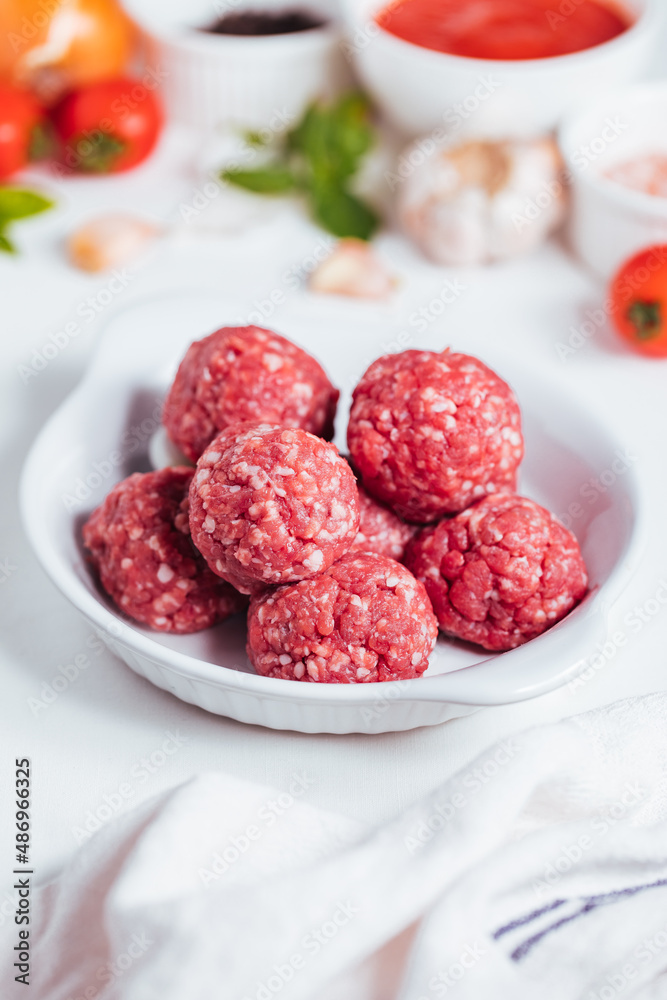 Meatballs in tomato sauce with basil on top. Bright background with ingredients in blurry background. This meal is called Kofte in Turkey and Cufte in Balkans. International meatball day. Meatballs in tomato sauce with basil on top. Bright background with ingredients in blurry background. This meal is called Kofte in Turkey and Cufte in Balkans. International meatball day.