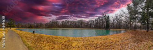фотографія a panoramic shot of a still green lake surrounded by yellow winter grass and bar