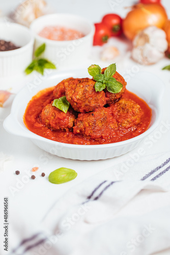 Meatballs in tomato sauce with basil on top. Bright background with ingredients in blurry background. This meal is called Kofte in Turkey and Cufte in Balkans. International meatball day.