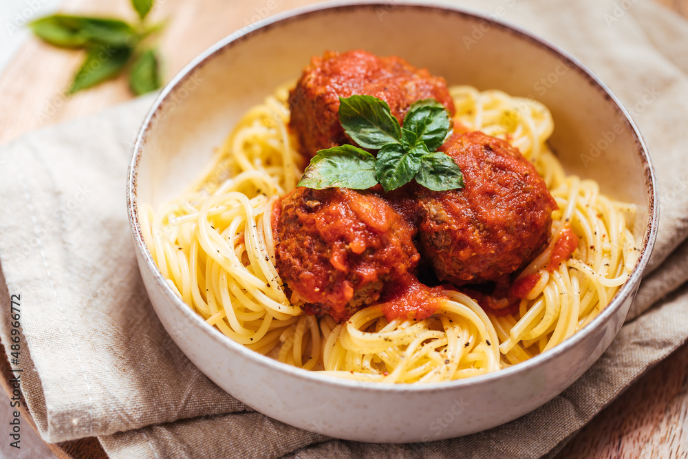 Meatballs in tomato sauce with basil on top. Bright background with ingredients in blurry background. This meal is called Kofte in Turkey and Cufte in Balkans. International meatball day. Meatballs in tomato sauce with basil on top. Bright background with ingredients in blurry background. This meal is called Kofte in Turkey and Cufte in Balkans. International meatball day.