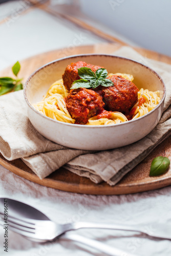 Meatballs in tomato sauce with basil on top. Bright background with ingredients in blurry background. This meal is called Kofte in Turkey and Cufte in Balkans. International meatball day.