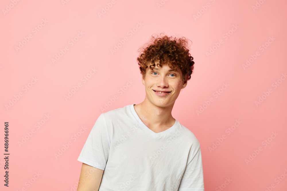 Young curly-haired man posing youth style white t-shirt pink background unaltered Young curly-haired man posing youth style white t-shirt pink background unaltered