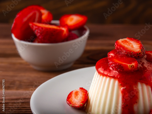 White panna cotta with strawberry in a dish on a wooden background