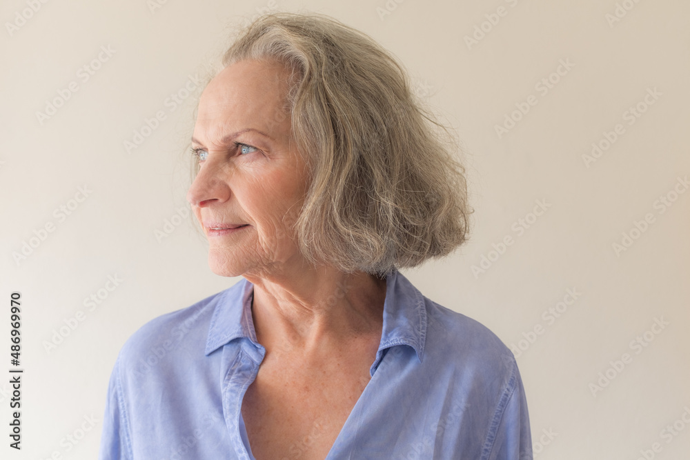 Profile view of older woman with grey hair and blue shirt against neutral wall background (selective focus) Profile view of older woman with grey hair and blue shirt against neutral wall background (selective focus)