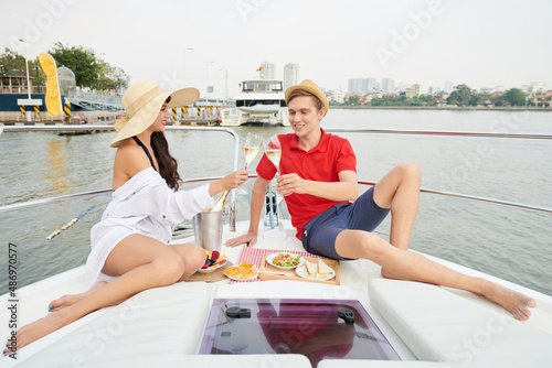 Positive young couple drinking champagne and eating fruits and snacks on yacht bow © DragonImages