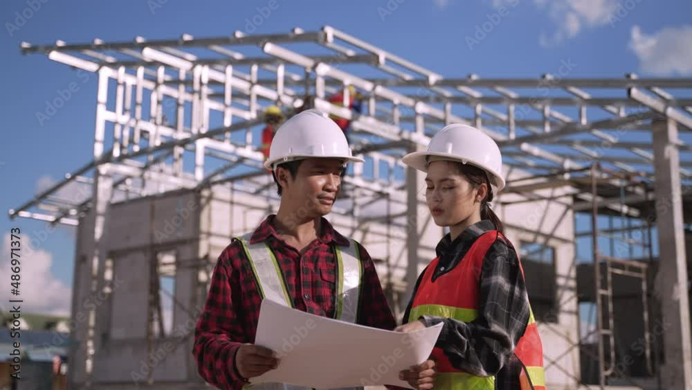 Two Asian man and woman engineer wears white safety helmet stand hold blueprint and radio while checking build in the construction site. Female architects and male civil specialists work on projects. 