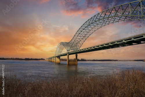 a gorgeous shot of the metal Memphis-Arkansas Bridge over the vast flowing waters of Mississippi river with powerful clouds and a stunning sky at sunset at Mud Island Park in Memphis Tennessee USA