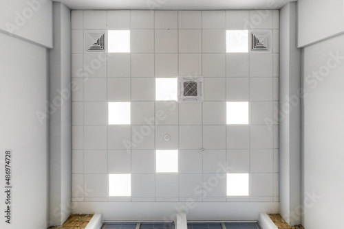 cassette suspended ceiling with square halogen spots lamps and drywall construction in empty room in apartment or house. Stretch ceiling white and complex shape. Looking up view