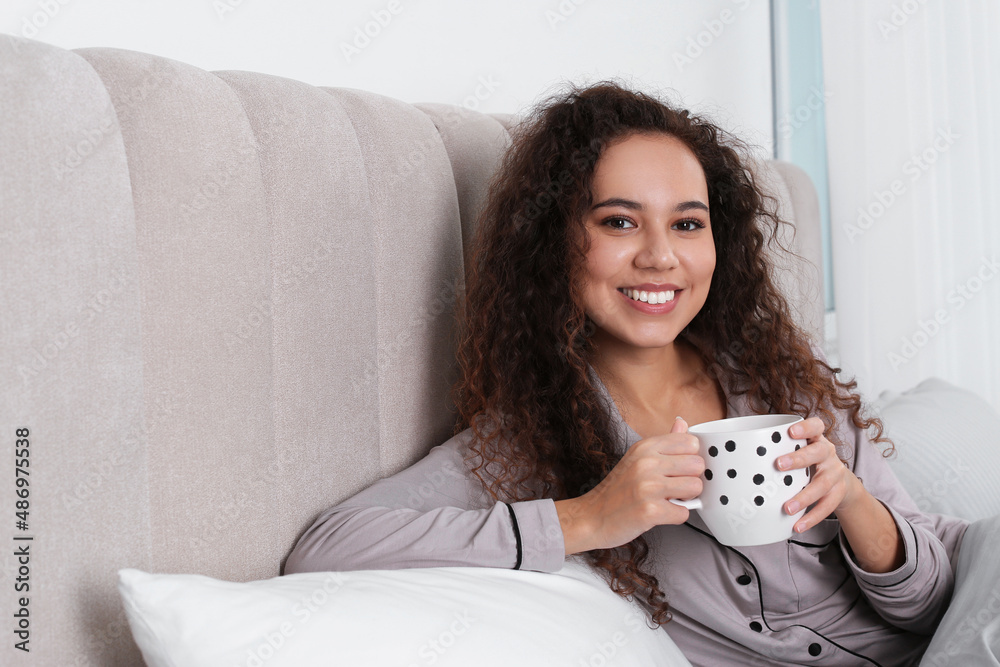 Beautiful African American woman with cup of drink in bed at home Beautiful African American woman with cup of drink in bed at home