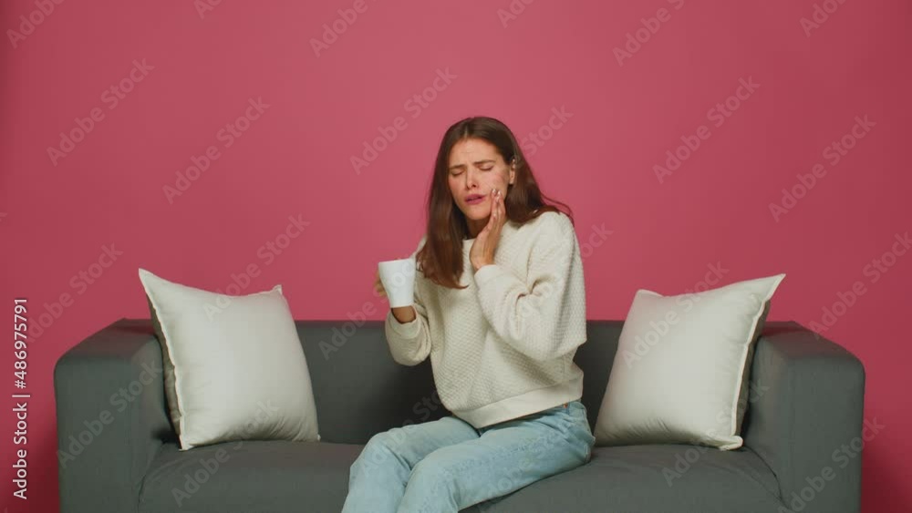Young girl suffer tooth ache, sensitive enamel, drinking hot tea, sitting on sofa. Dental clinic, medical insurance ad Young girl suffer tooth ache, sensitive enamel, drinking hot tea, sitting on sofa. Dental clinic, medical insurance ad