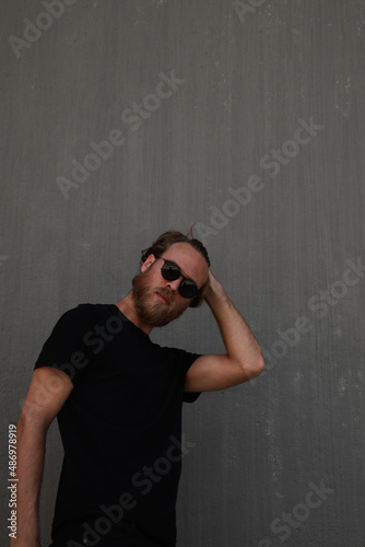 Portrait of bearded man posing over dark background wears black t-shirt.
