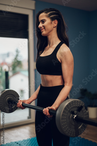 Beautiful athletic woman lifting barbell while training in the gym