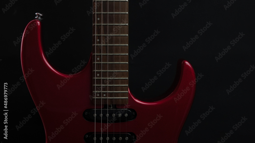 Fototapeta premium A red shiny electric guitar standing upright on black background as wallpaper. Music concept