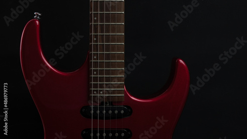 A red shiny electric guitar standing upright on black background as wallpaper. Music concept