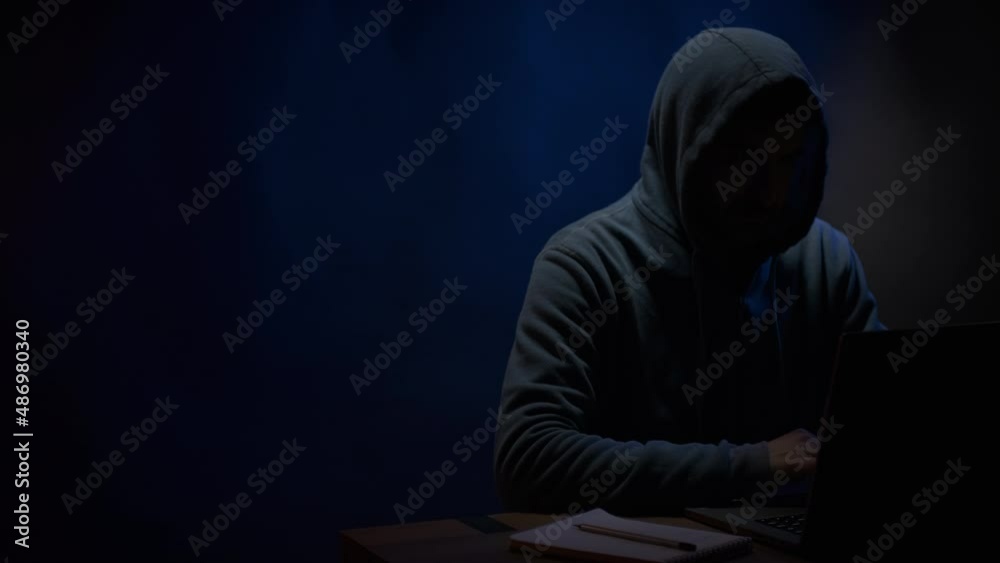 Hacker near front of computer laptop. Man hacker in dark room background Hacker near front of computer laptop. Man hacker in dark room background