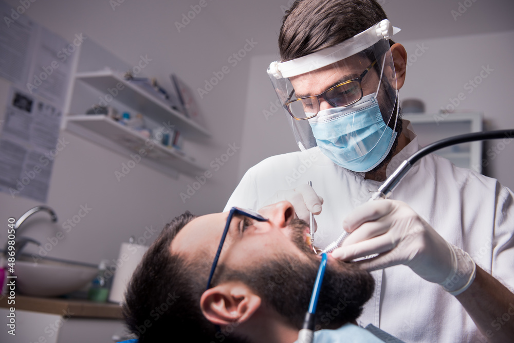 Dentist drilling a tooth with a turbine. Saliva ejector is placed in a