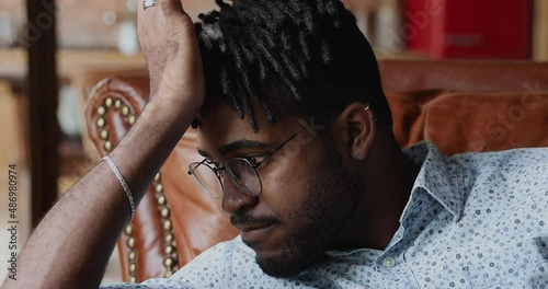 Close up view thoughtful doubtful African hipster man prop head with hand lost in thoughts hesitate ponder on important decision choice. Pensive young guy contemplate on work life problem feel unsure photo