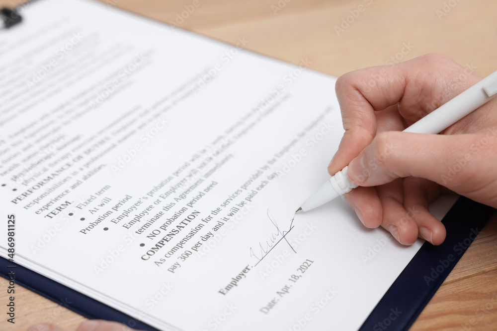 Woman signing contract at wooden table, closeup. Woman signing contract at wooden table, closeup.