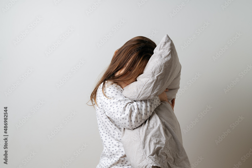 Portrait of pretty caucasian girl in white pyjama and pillow in studio white background 
