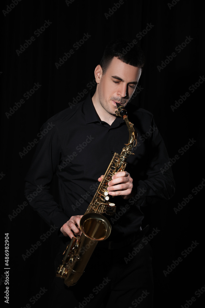 Fototapeta premium Young man playing saxophone on dark background