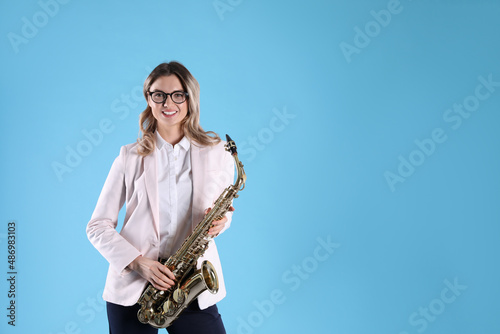 Beautiful young woman in elegant outfit with saxophone on light blue background. Space for text