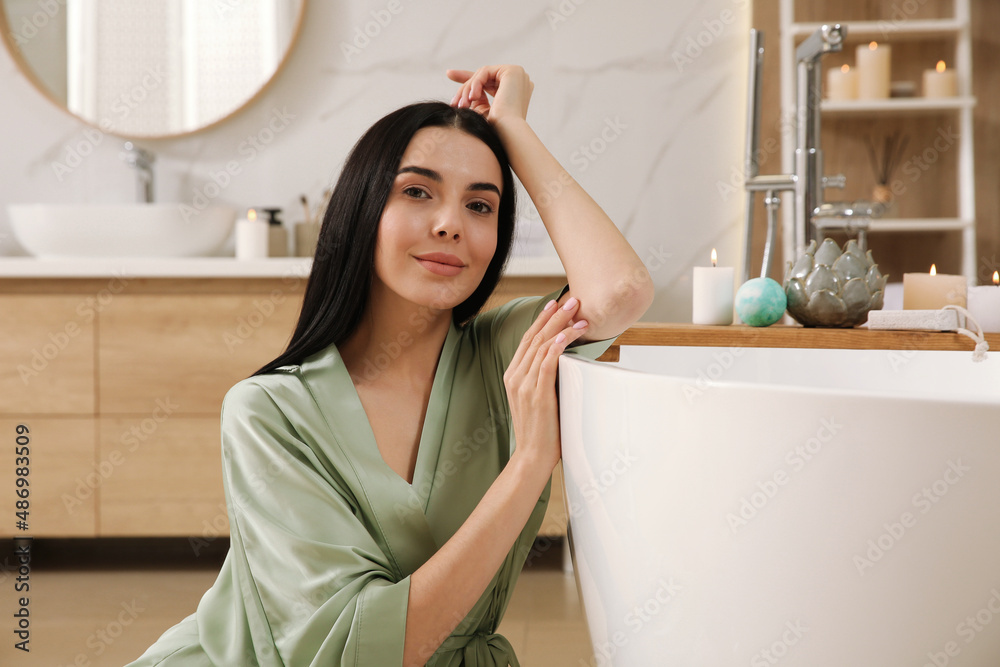 Beautiful young woman sitting near tub in bathroom Beautiful young woman sitting near tub in bathroom