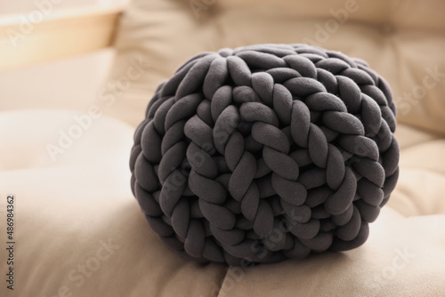 Dark grey chunky knitted pillow on beige sofa, closeup