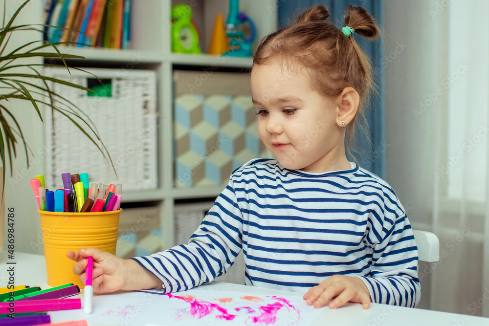 A beautiful little girl sits at a table at home and draws. Development of preschoolers. A beautiful little girl sits at a table at home and draws. Development of preschoolers.