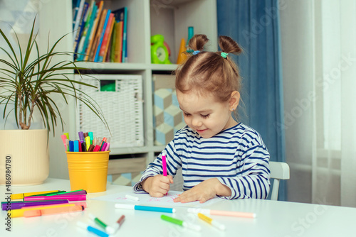 A beautiful little girl sits at a table at home and draws. Development of preschoolers.