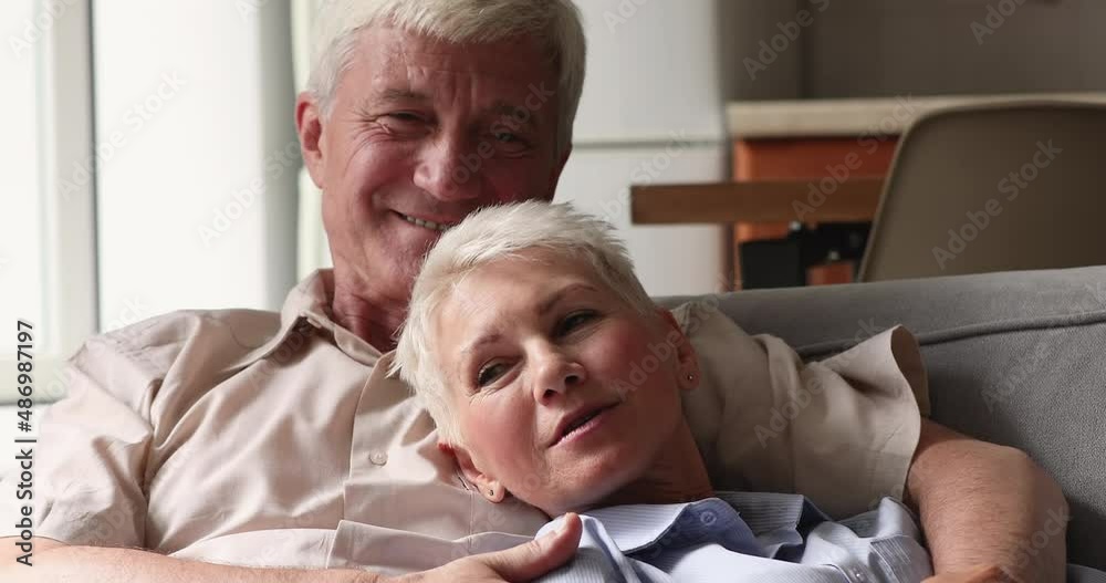Smiling mature couple in love talking relaxing on sofa at home. Positive peaceful older spouses having pleasant conversation speak sit on couch in living room. Romance, relation, communication concept Smiling mature couple in love talking relaxing on sofa at home. Positive peaceful older spouses having pleasant conversation speak sit on couch in living room. Romance, relation, communication concept