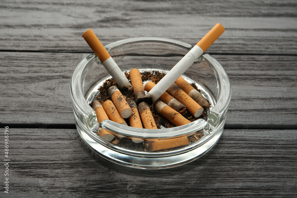 Glass ashtray with cigarette stubs on black wooden table Glass ashtray with cigarette stubs on black wooden table