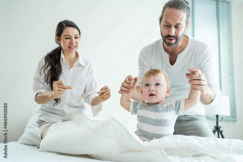 Caucasian loving parents play with baby boy child on bed in bedroom. Caucasian loving parents play with baby boy child on bed in bedroom.