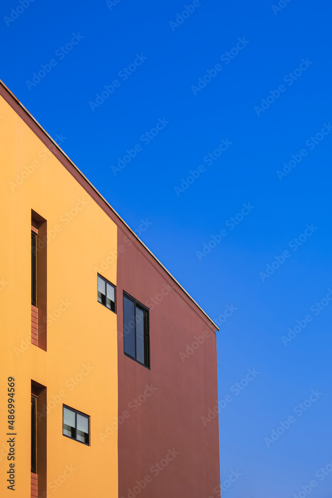 Side view of various fixing glass windows on orange and brown wall of modern house against blue clear sky in minimal style and vertical frame 