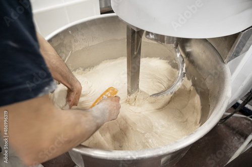 Baker taking out dough of a kneading machine at industrial bakery. High quality photography photo