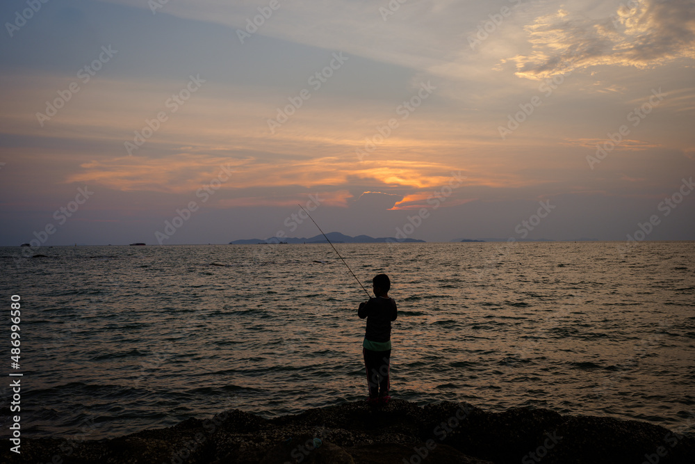 Silhouette little boy fishing on the beach at dusk.