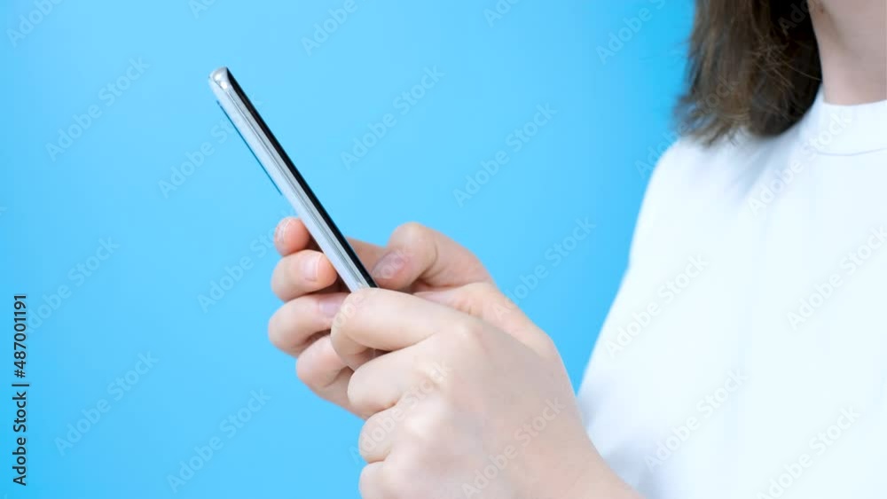 Female hands are typing on smartphone close up on blue background. Female hands are typing on smartphone close up on blue background.