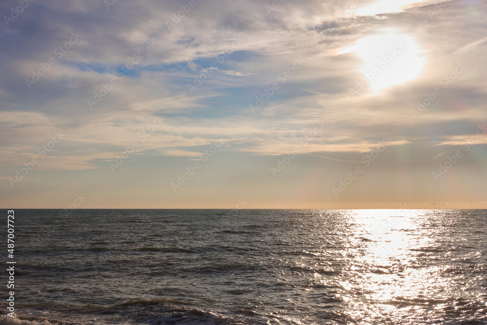 Fototapeta premium Gray stormy sea at sunset. In a cloudy sky, the sun goes down below the horizon.
