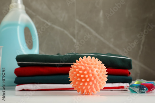 Orange dryer ball near stacked clean clothes  laundry detergents on white table