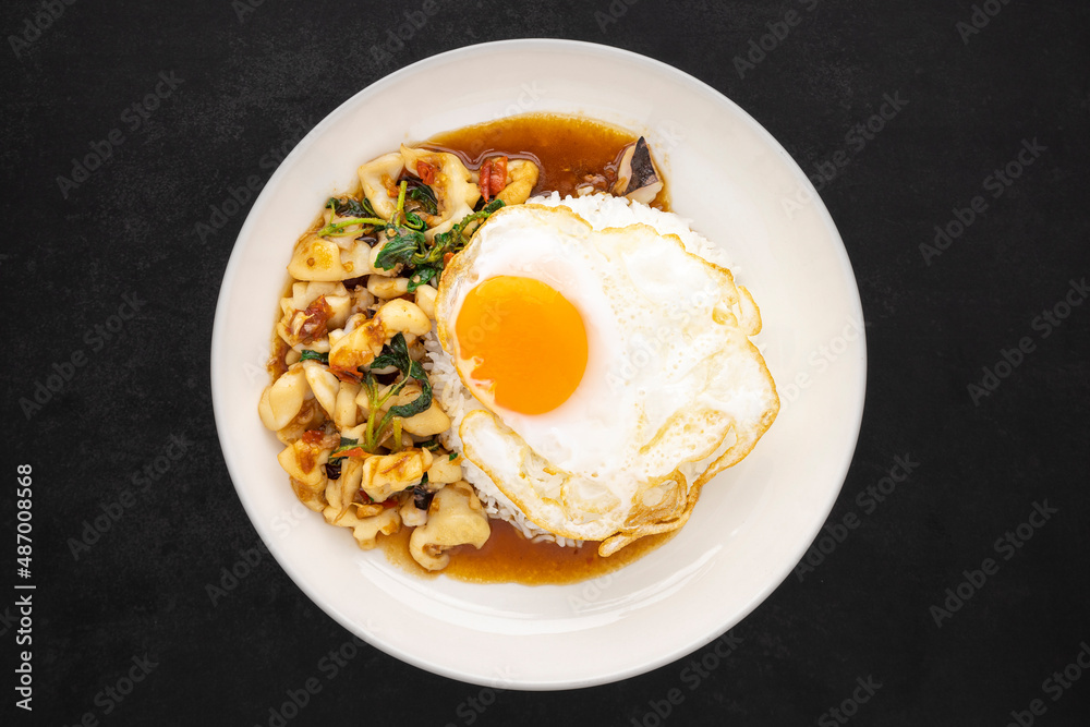 Khao Pad Ka Prao Pla Muek Kai Dao, Thai food, streamed rice topped with basil stir fried squid, octopus and fried egg in ceramic plate on dark tone texture background, top view, flat lay Khao Pad Ka Prao Pla Muek Kai Dao, Thai food, streamed rice topped with basil stir fried squid, octopus and fried egg in ceramic plate on dark tone texture background, top view, flat lay