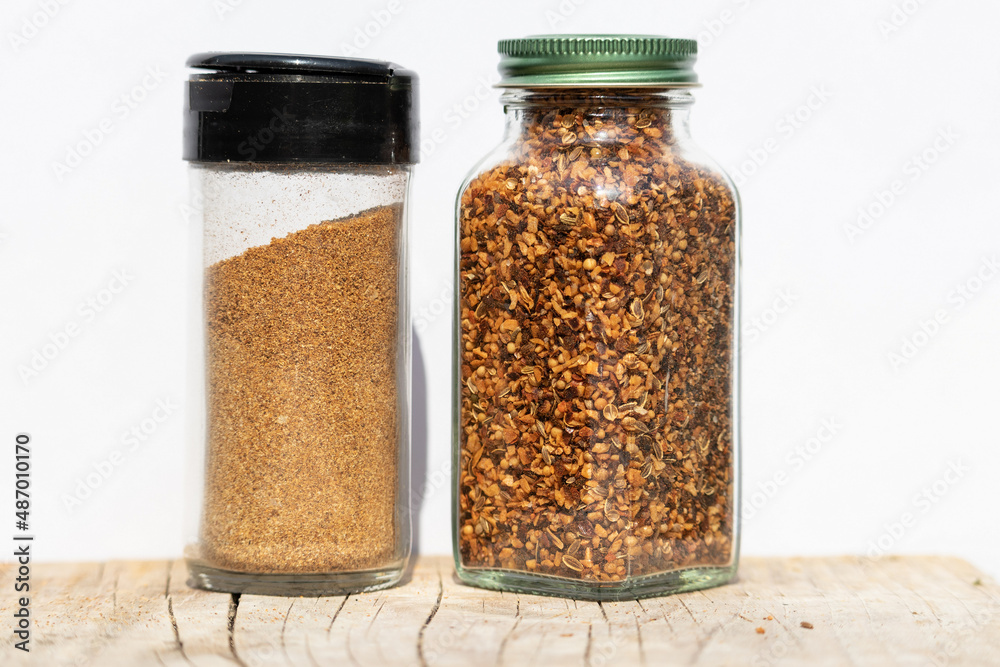 Two jars of differently ground spices on a wooden board and white background Two jars of differently ground spices on a wooden board and white background