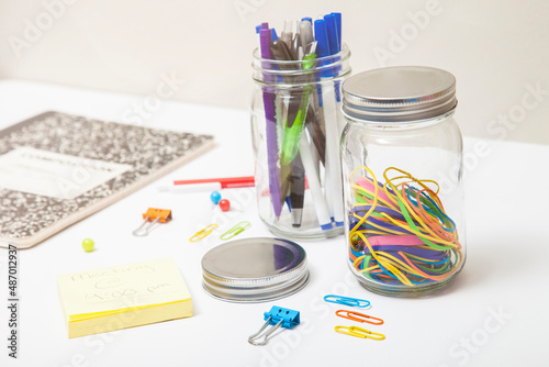 Clear Glass mason jars storing colorful office supplies on white desk