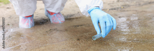 Environmentalist in protective suit and gloves taking water samples from lake closeup photo