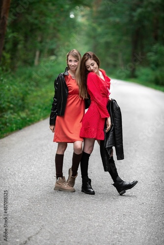 A girl in a light red airy dress, a leather jacket in a rockstyle on an empty road in a summer forest