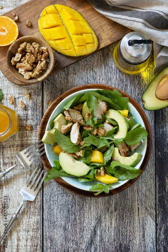 Healthy diet salad with chicken, arugula, mango, avocado and vinaigrette dressing on a rustic countertop. Top view flat lay background. Copy space.