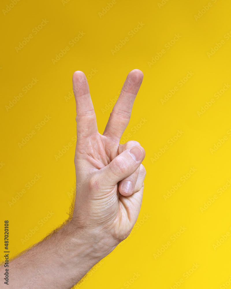 Naklejka premium Male two fingers up on hand gesture isolated on yellow background. Victory sign, V sumbol.