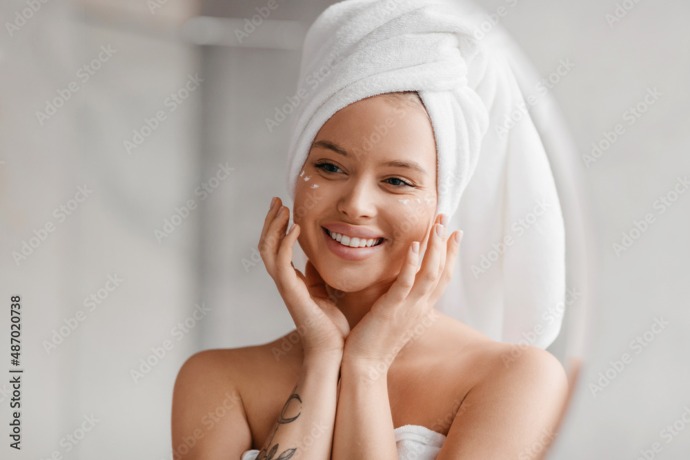 Mirror reflection of beautiful lady applying anti-aging or hydrating product on eyes zone after morning shower Mirror reflection of beautiful lady applying anti-aging or hydrating product on eyes zone after morning shower