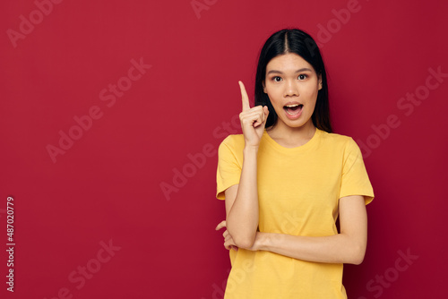Charming young Asian woman yellow casual t shirt smile posing red background unaltered